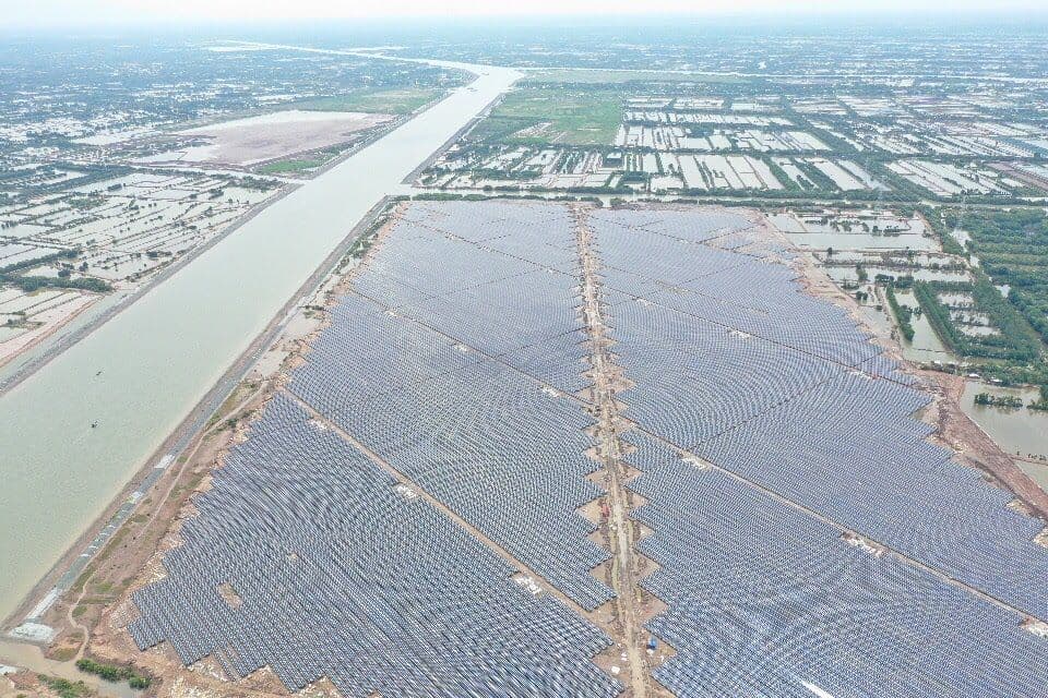 Aerial view of a vast solar farm alongside a wide canal under cloudy skies.