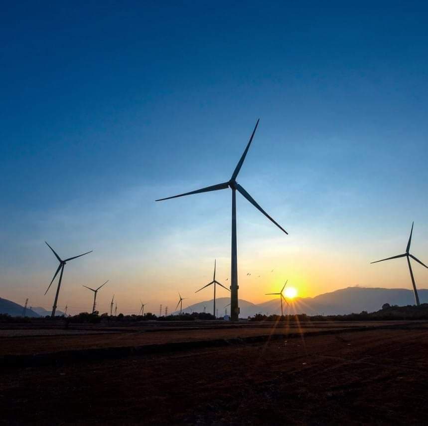Wind turbines silhouetted against a vibrant orange and blue sky at sunset.