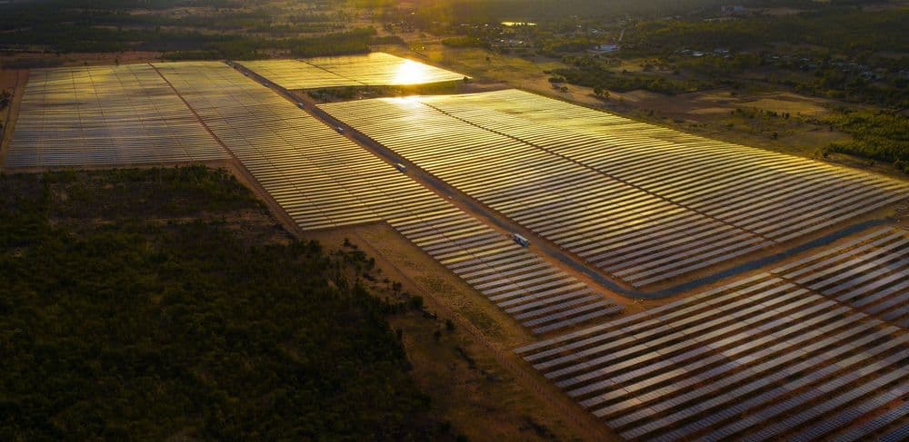 Aerial view of a vast solar farm with rows of panels reflecting golden sunlight at sunset.