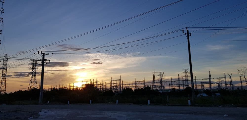 Sunset silhouetting power lines and an electrical substation against a colorful sky.