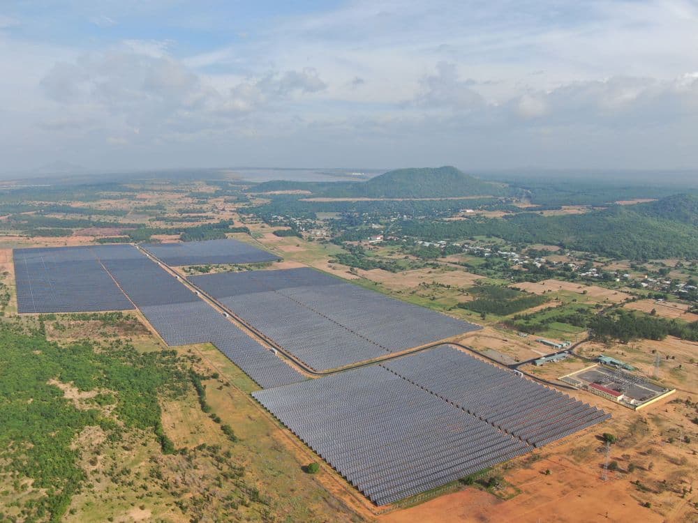 Aerial view of an extensive solar farm with vast arrays of panels in a natural landscape.