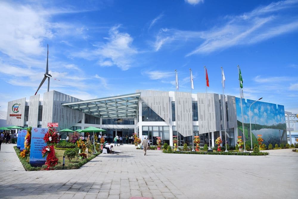 Modern building with a glass facade, wind turbine, and flags under a blue sky.