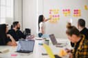 A woman points at colorful sticky notes on a whiteboard during a team brainstorming session.