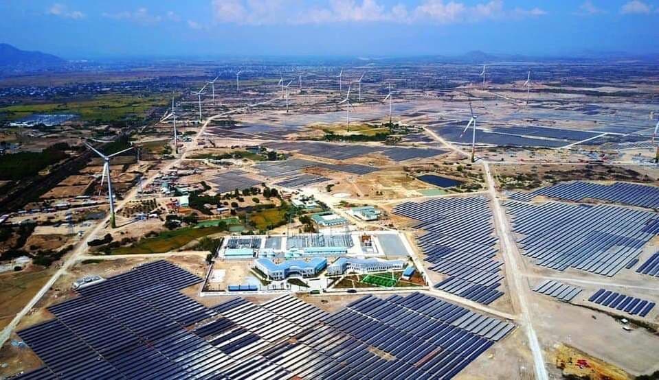 Aerial view of a vast hybrid solar and wind power farm with central facilities.