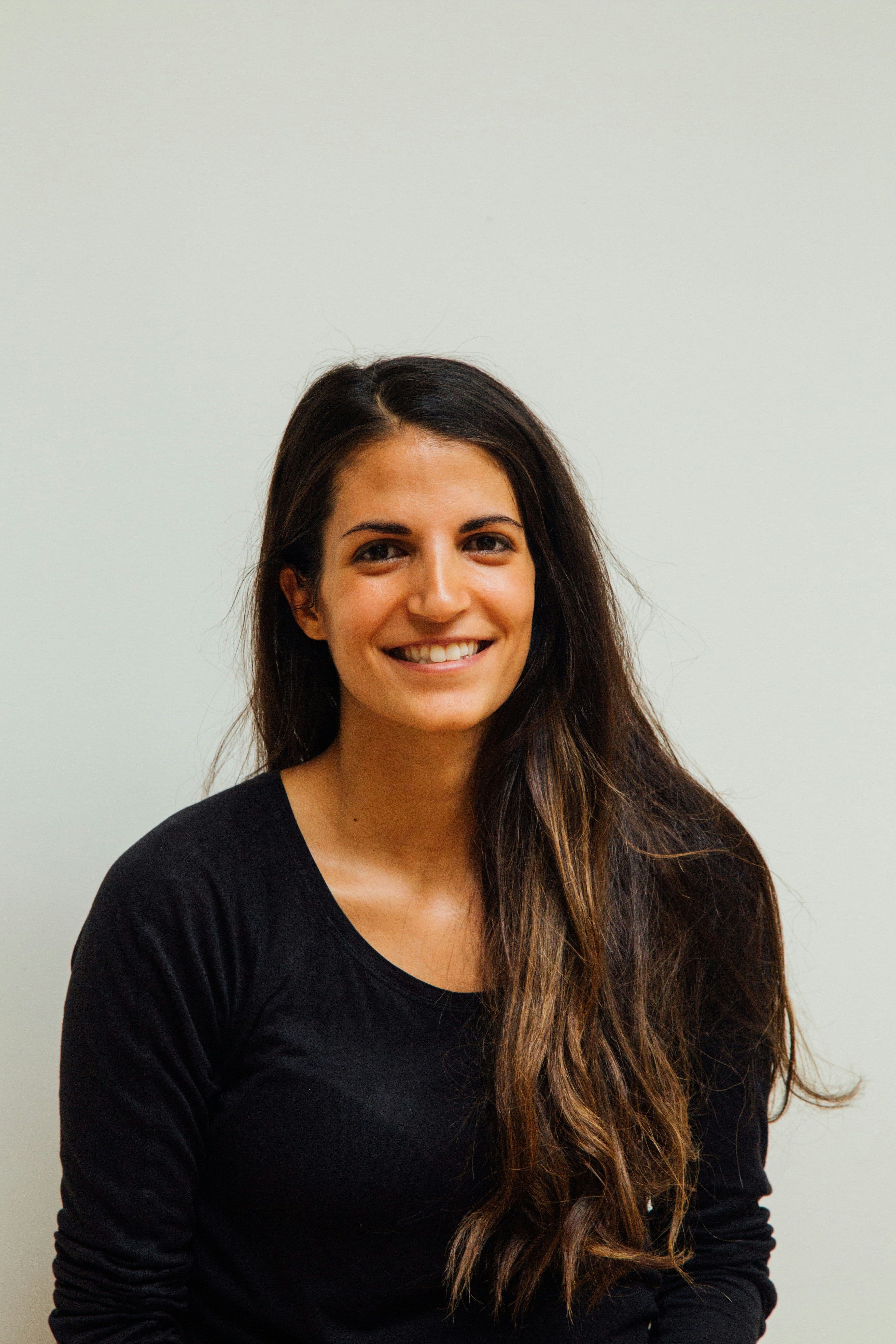 Smiling woman with long dark hair wearing a black shirt against a plain background.